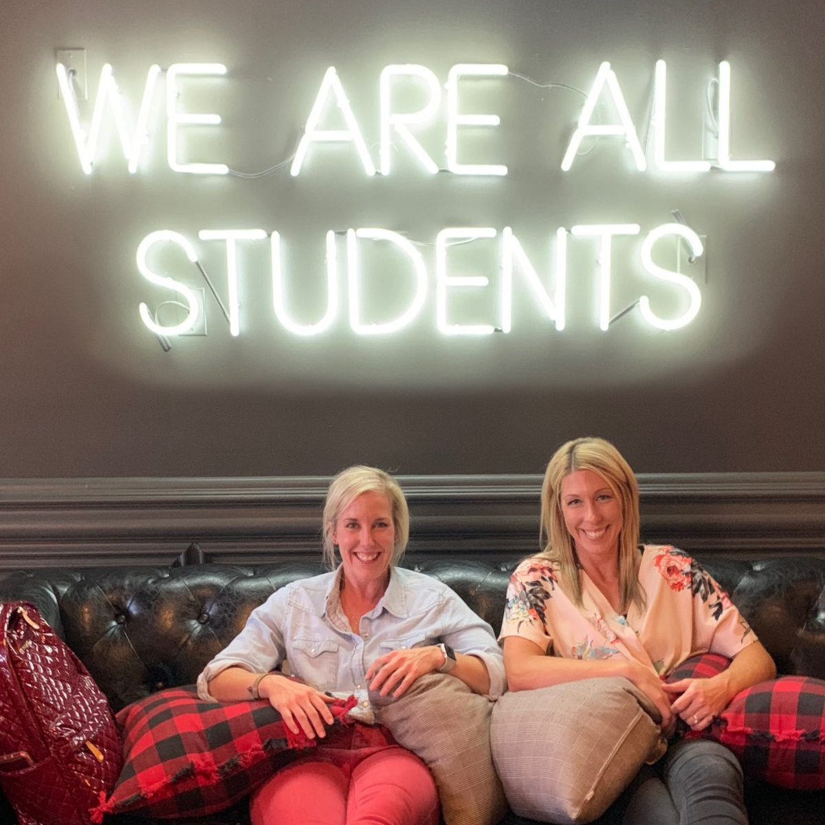 Erin and Stacy smiling on couch below sign that says 