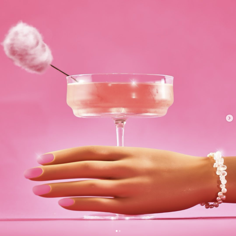 Barbie hand reaching for a pink drink with a cotton candy stirrer